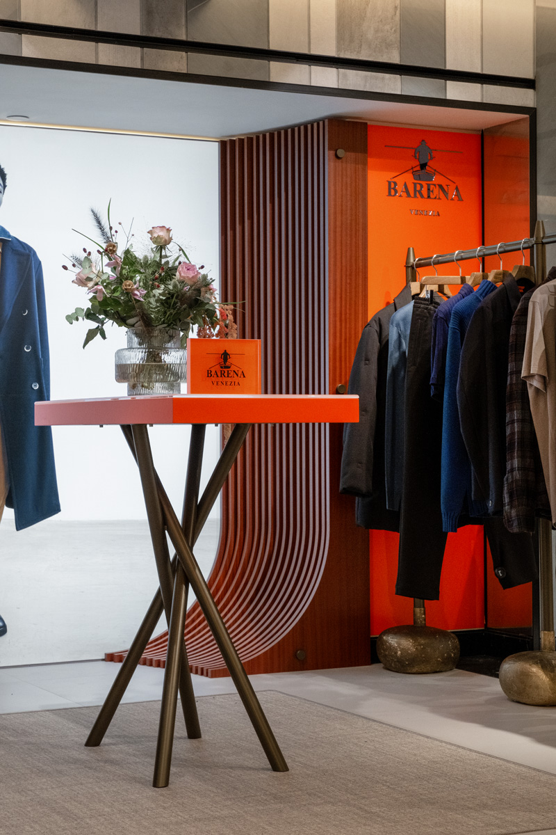 Pop-up Barena Venezia ad Harrods: tavolino arancione con fiori, capi maschili e pannello arancio brand