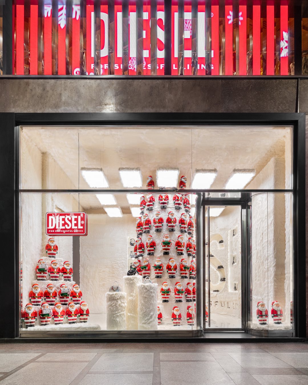 Vetrina natalizia Diesel: piramide di babbi natale e insegna rossa luminosa For Successful Living