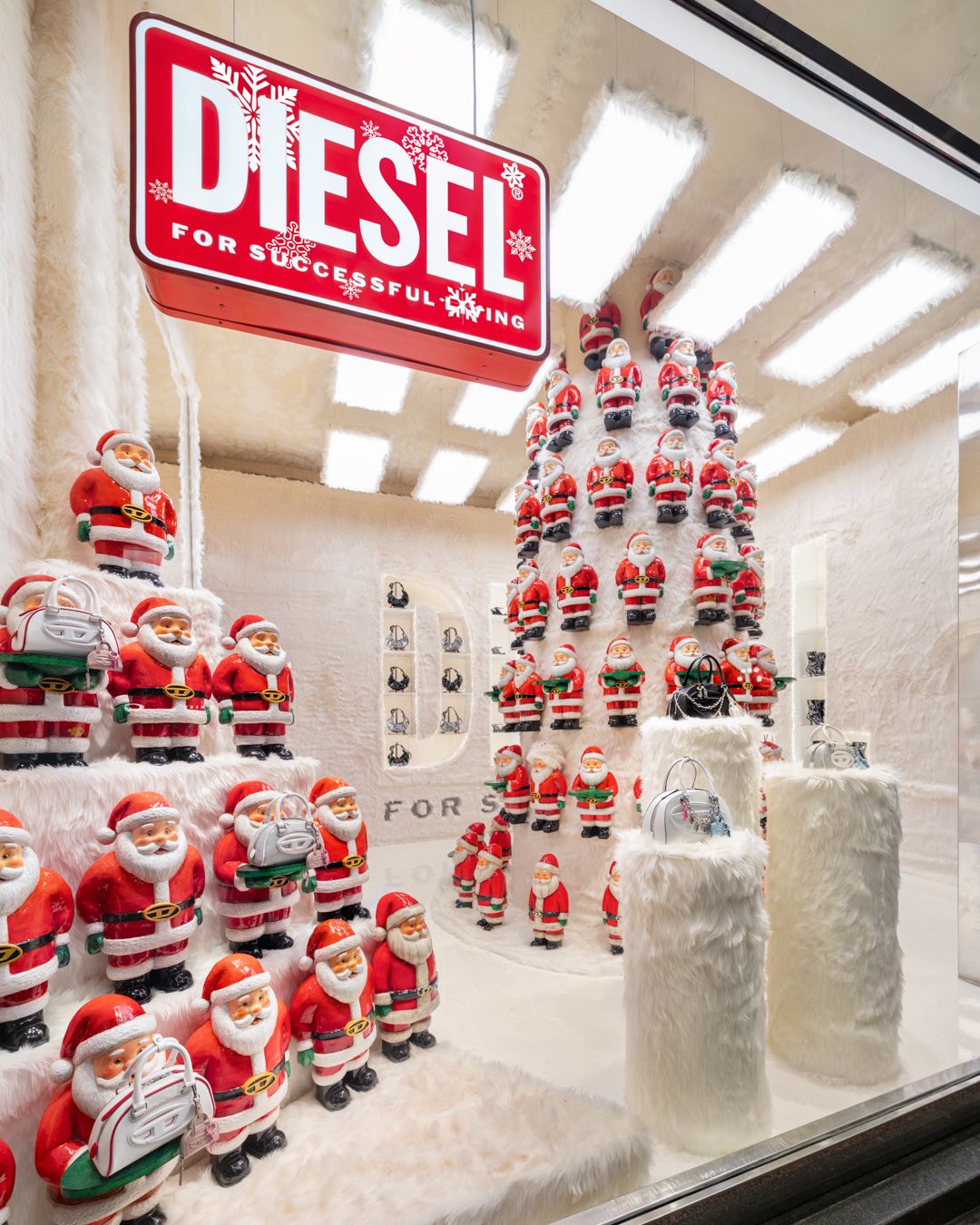 Vetrina Natale Diesel For Successful Living con piramide di Babbi Natale rossi e neve sintetica