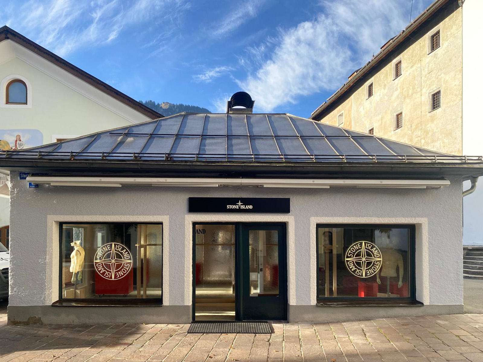 Esterno boutique Stone Island a Kitzbühel con rosone logo dorato e insegna nera