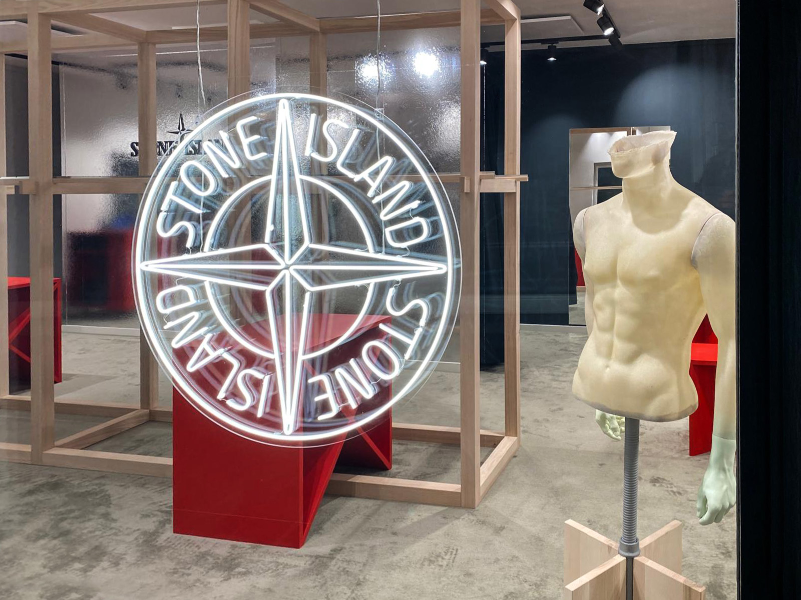 Vetrina Stone Island Kitzbühel con maxi logo bussola al neon e mezzo manichino in cera