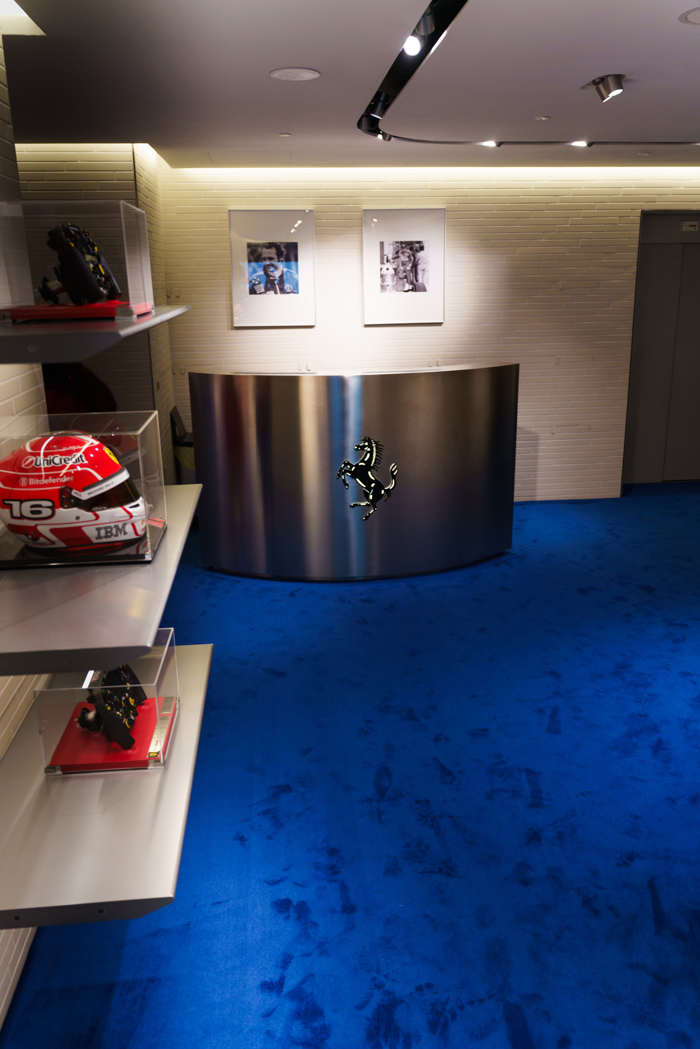 Reception Ferrari boutique con cavallino rampante, moquette blu e teche con caschi da pilota