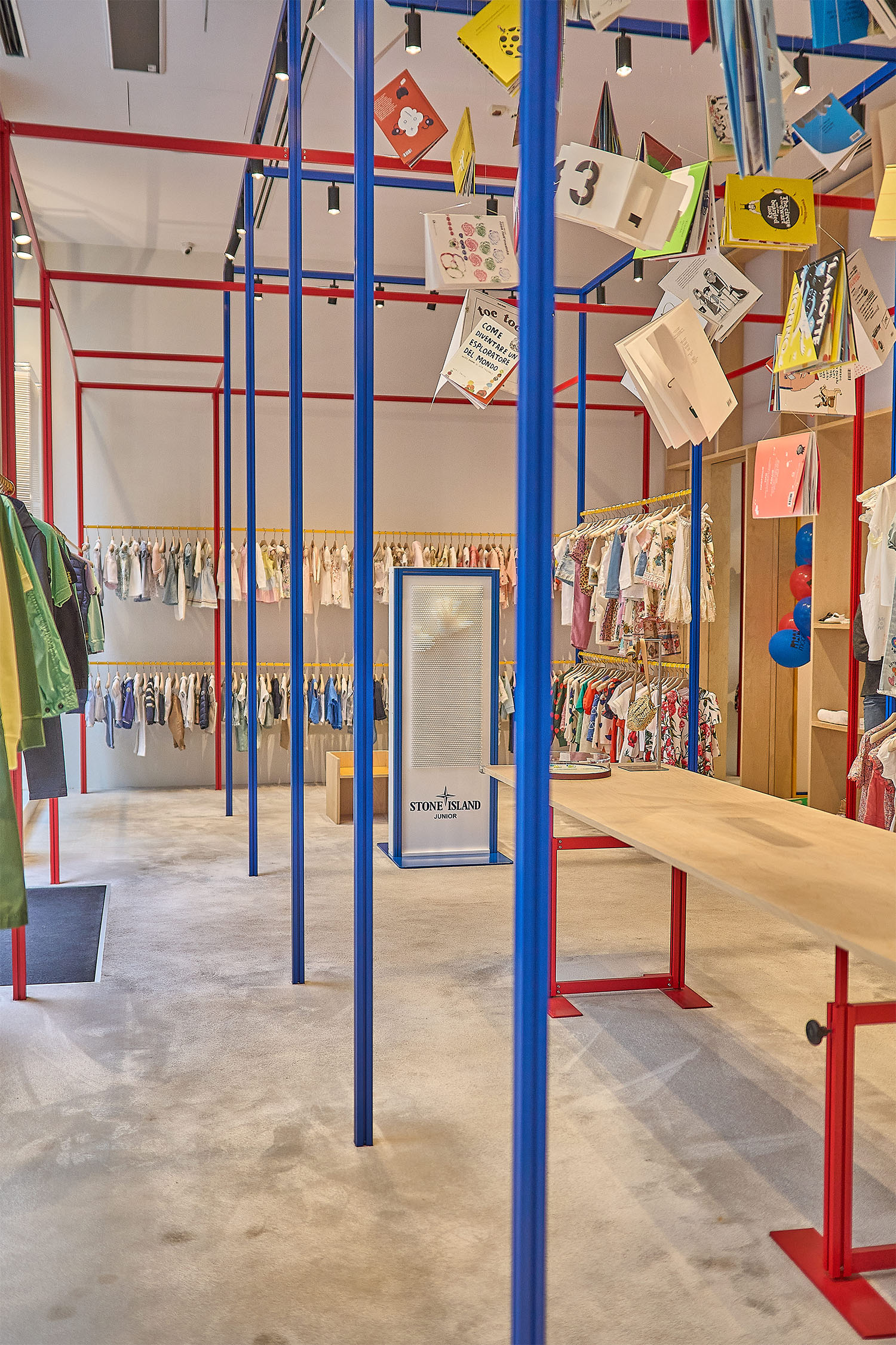 Allestimento Stone Island Mini Modes Milano: struttura tubolare blu e rossa con cartellini sospesi